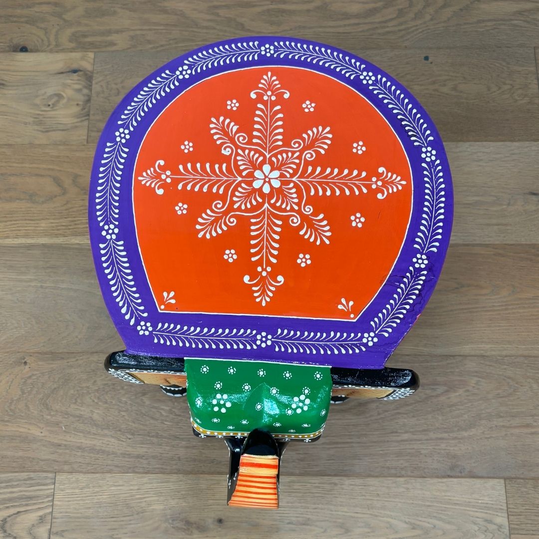 Top view of the wooden elephant stool showcasing its smooth round tabletop and orange & purple finish