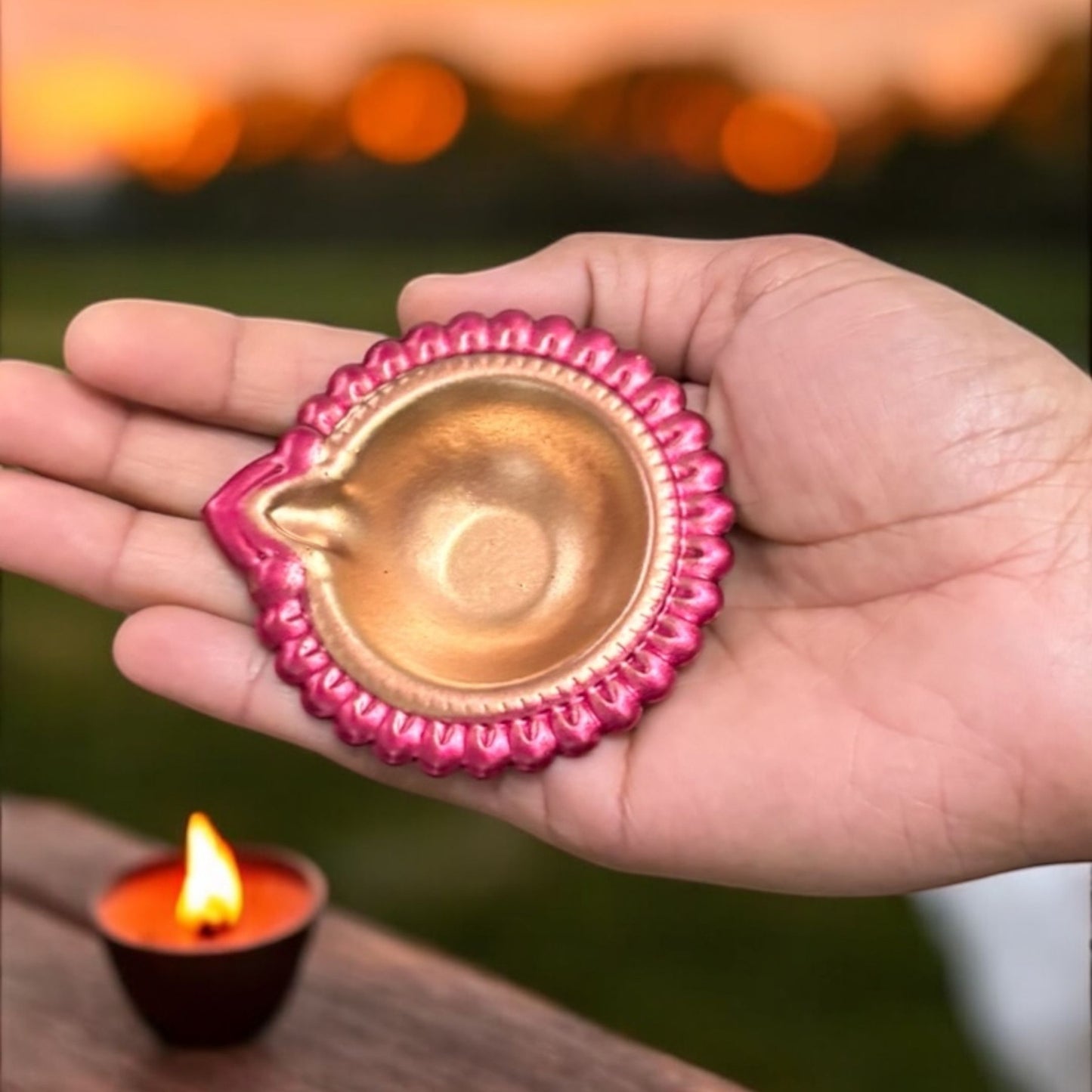 Hand holding a pink metal diwali diya, demonstrating its compact size and portability for various decor uses
