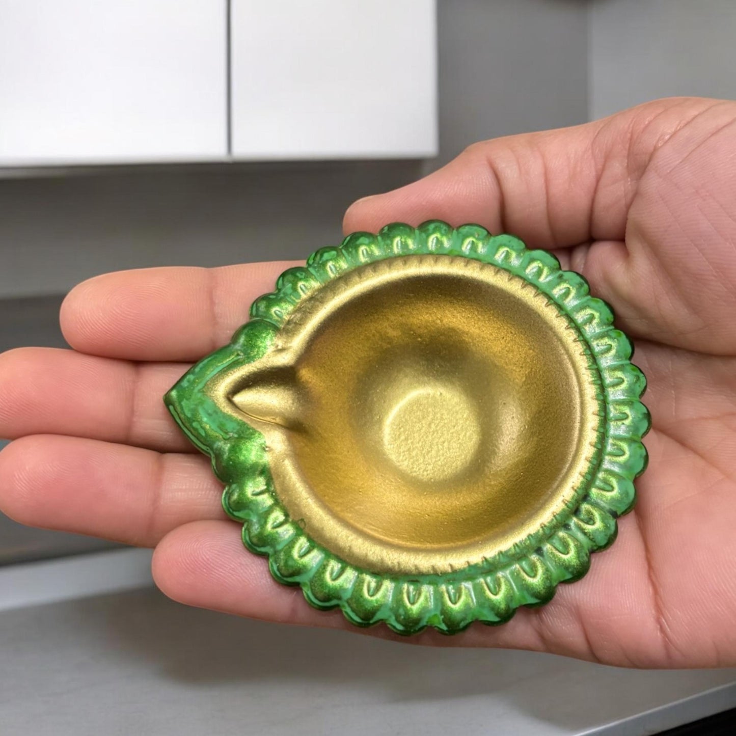 Hand holding a green metal diwali diya, demonstrating its compact size and portability for various decor uses