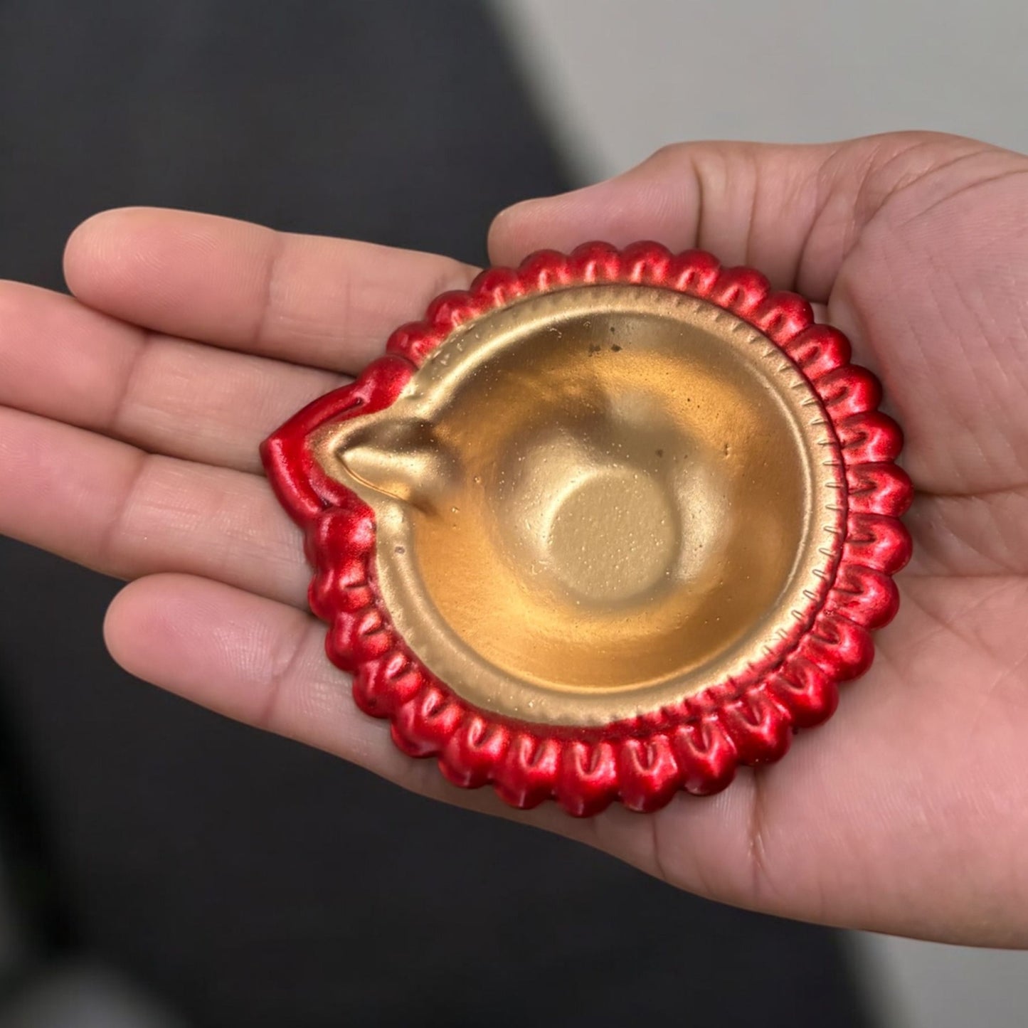 Hand holding a red metal diwali diya, demonstrating its compact size and portability for various decor uses