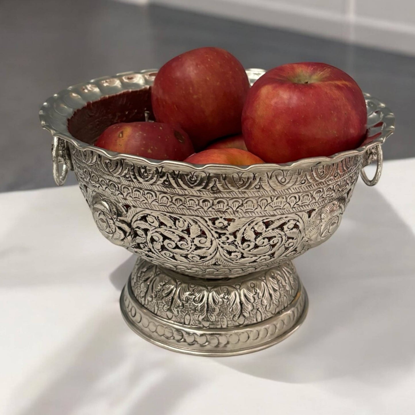 The antique silver fruit bowl filled with an assortment of colorful fruits, highlighting its functionality and aesthetic appeal as a centerpiece