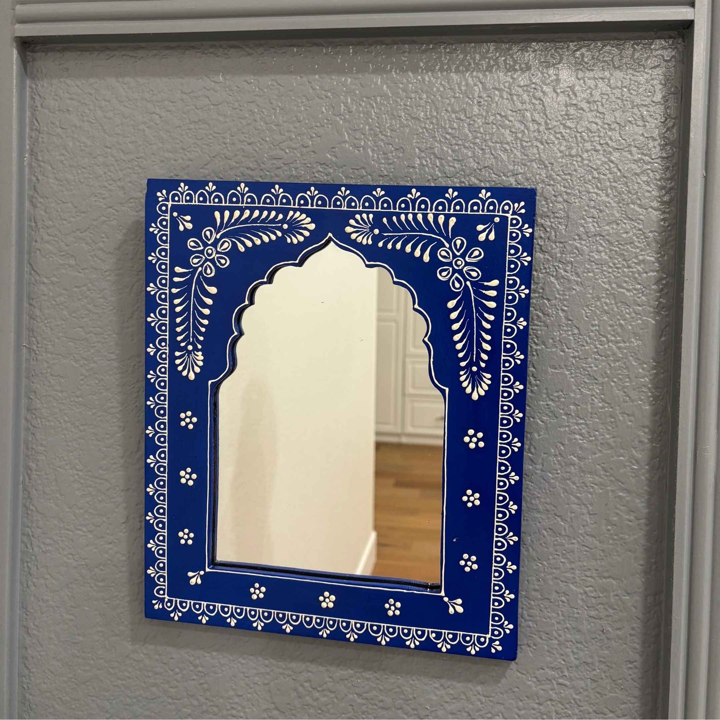 The 12x10-inch Blue Jharokha mirror from Urli Utsav displayed on a wall, illustrating its decorative appeal in a home setting