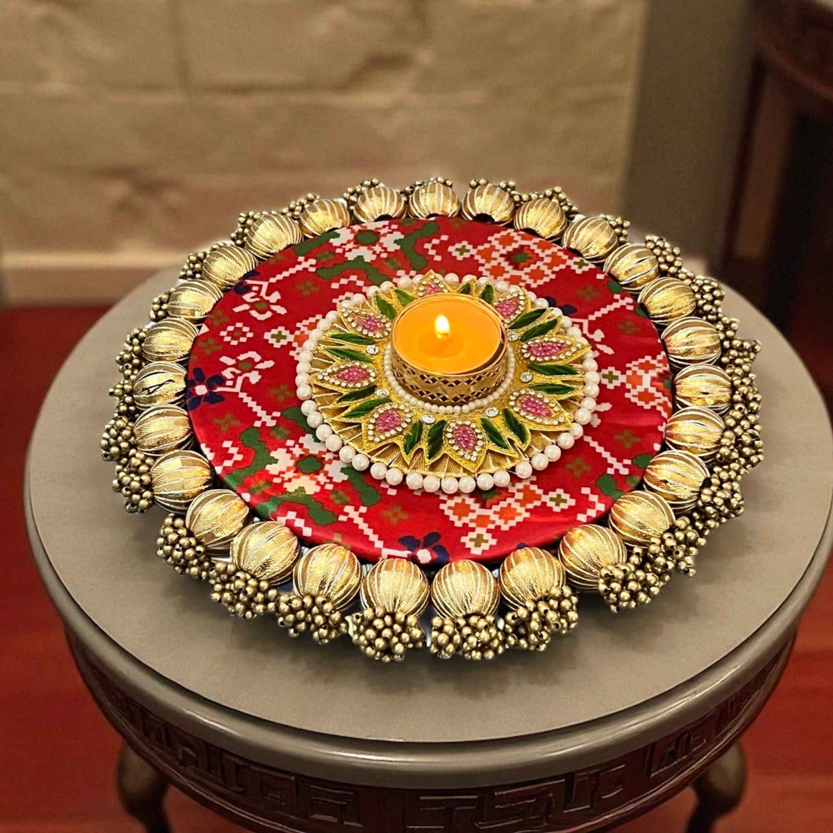 Close-up of a lit diya with a gold beaded border and floral center on red bandhani-pattern fabric