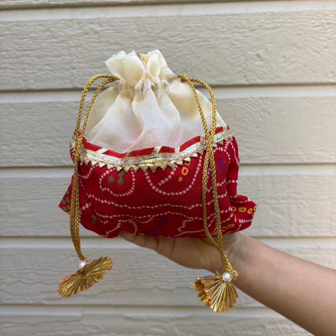 Hand holding a red and gold decorative bag with tassels against a beige wall.