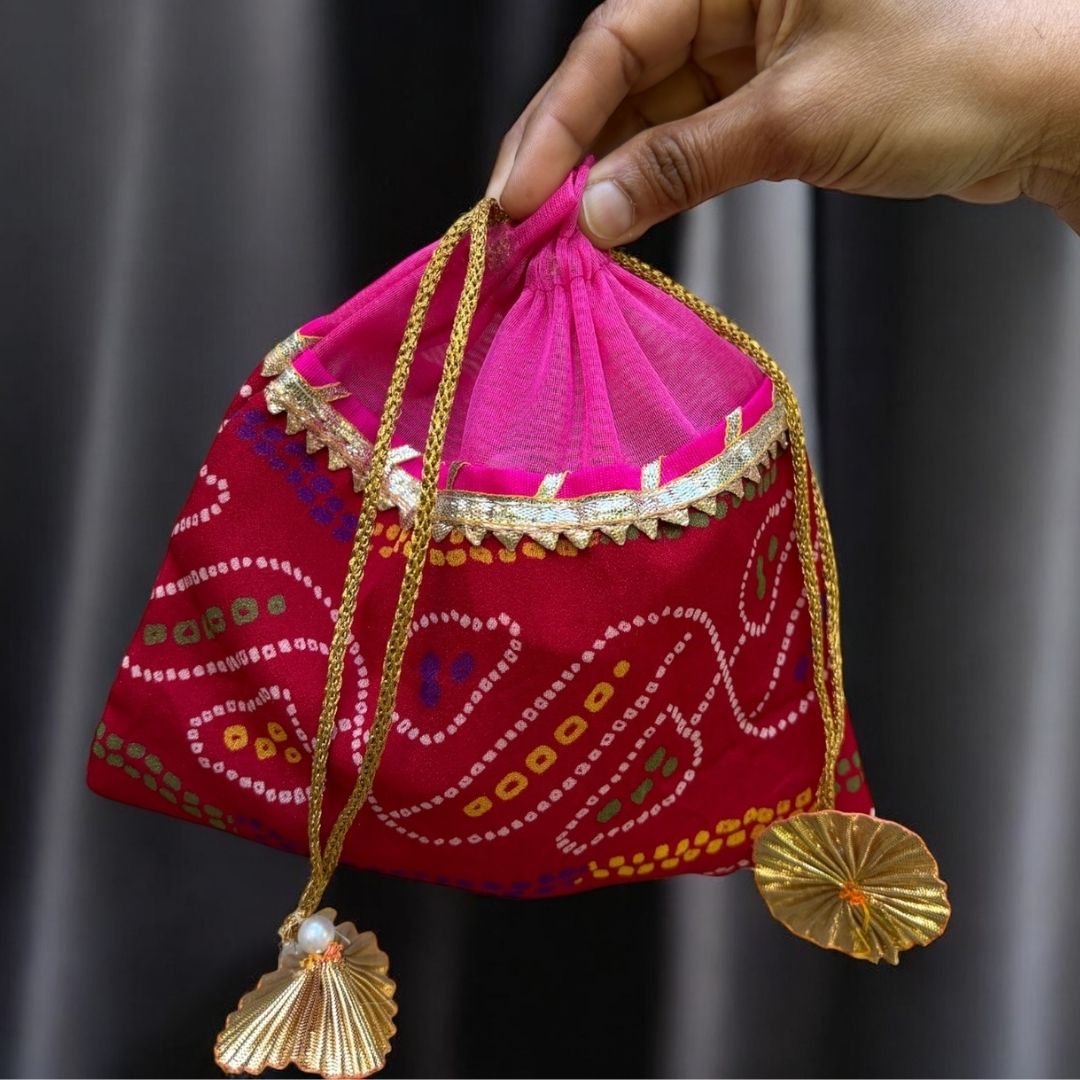 Decorative pink and red bag with gold accents held by a hand against a dark background