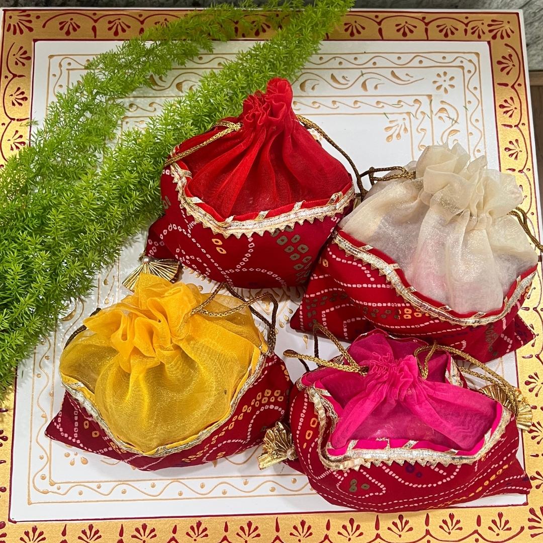 Decorative fabric bags in red, yellow, and pink on a patterned surface with greenery.