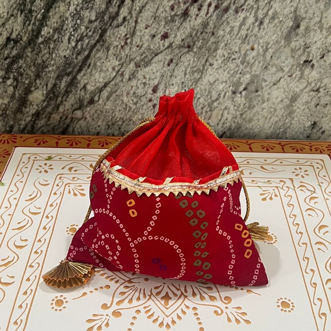 Red fabric pouch with gold patterns on a decorative surface with a stone wall background