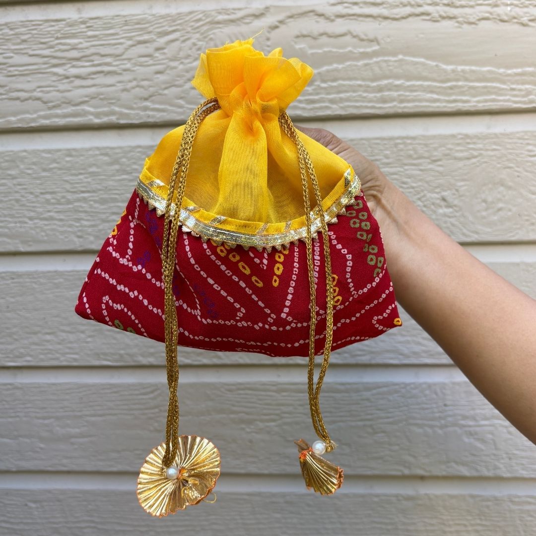 Hand holding a red and yellow fabric pouch with decorative elements against a neutral background