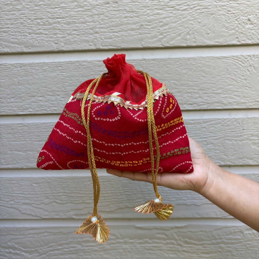 Red fabric pouch with gold embroidery held by a hand against a beige wall.