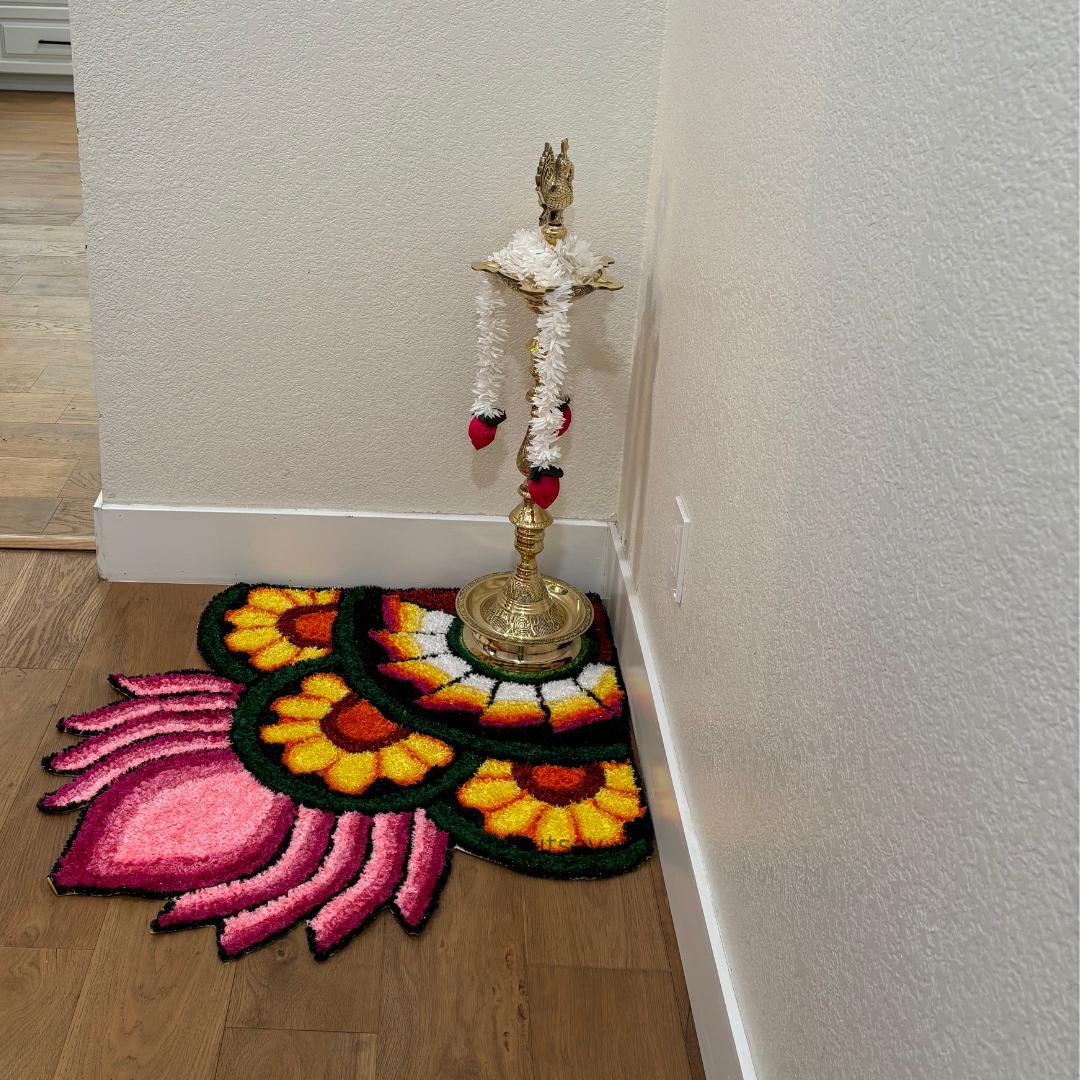 Indoor shot of a corner decorated with layered rangoli mats in warm yellow, orange, and pink hues, placed beside a brass lamp holder