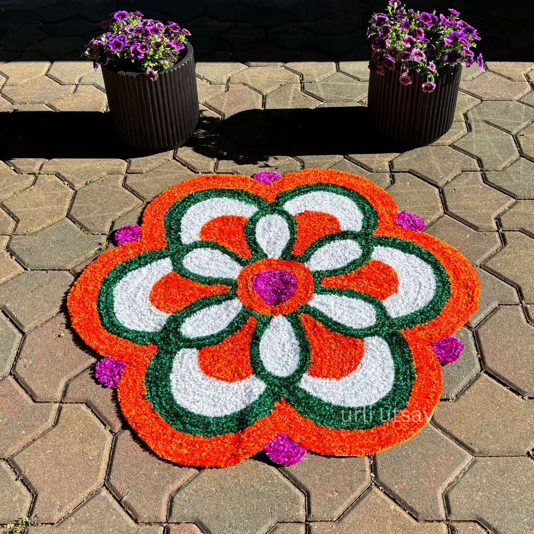 Close-up of a single red-and-white floral rangoli mat on a paved courtyard, showcasing a symmetrical petal pattern
