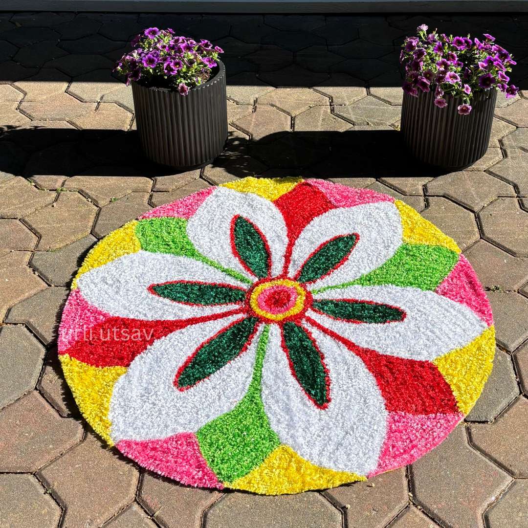 Bright rangoli mat featuring oversized white petals with colorful border, placed indoors near a wall