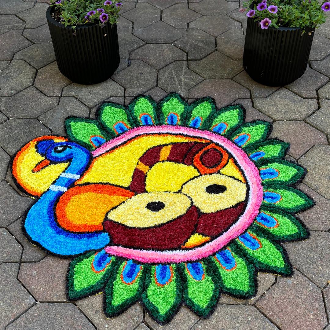 Vibrant peacock-themed rangoli mat with green feathered edge and stylized peacock central motif, displayed on outdoor stone floor.