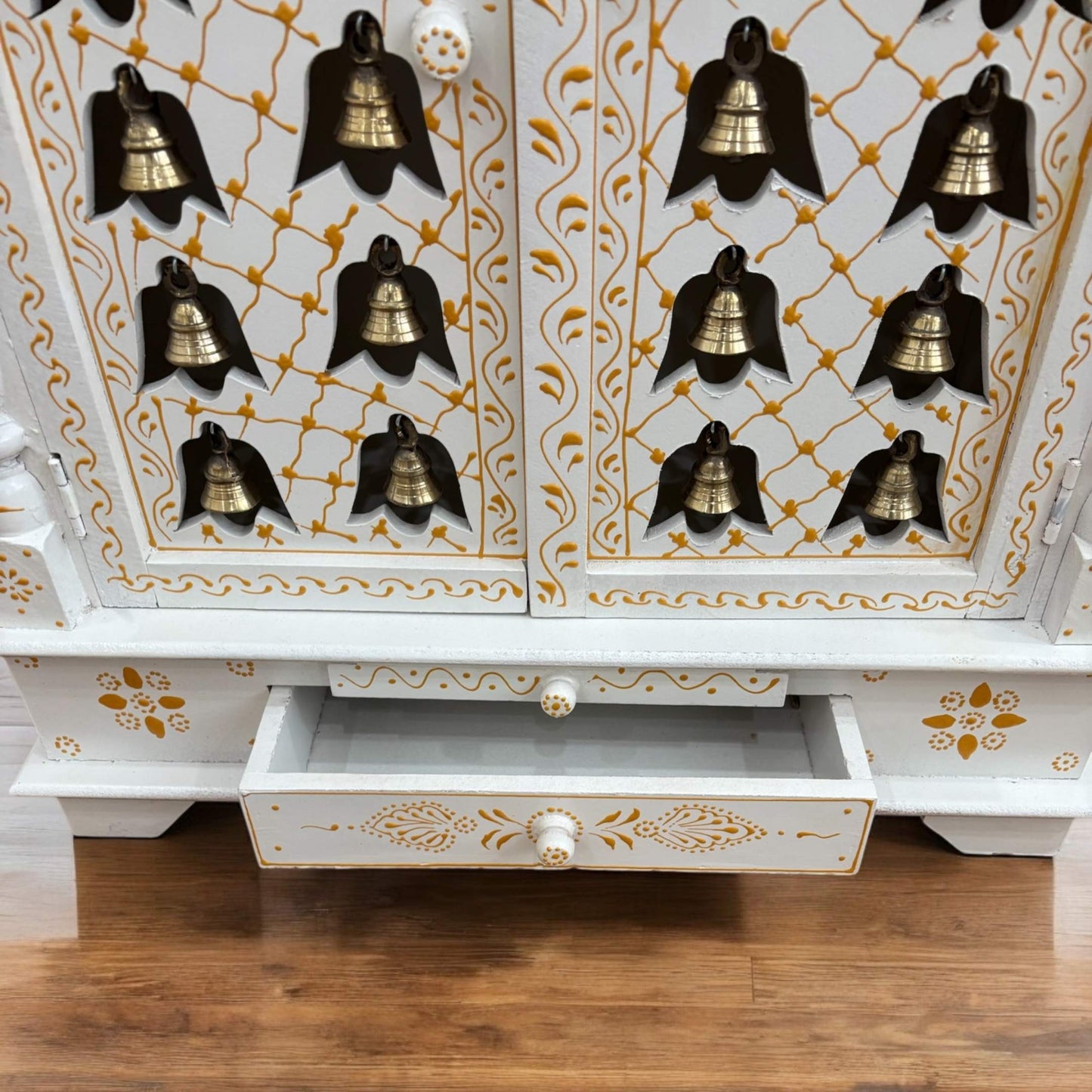 Front view of the handcrafted white and gold wooden temple with intricate carvings and brass hanging bells