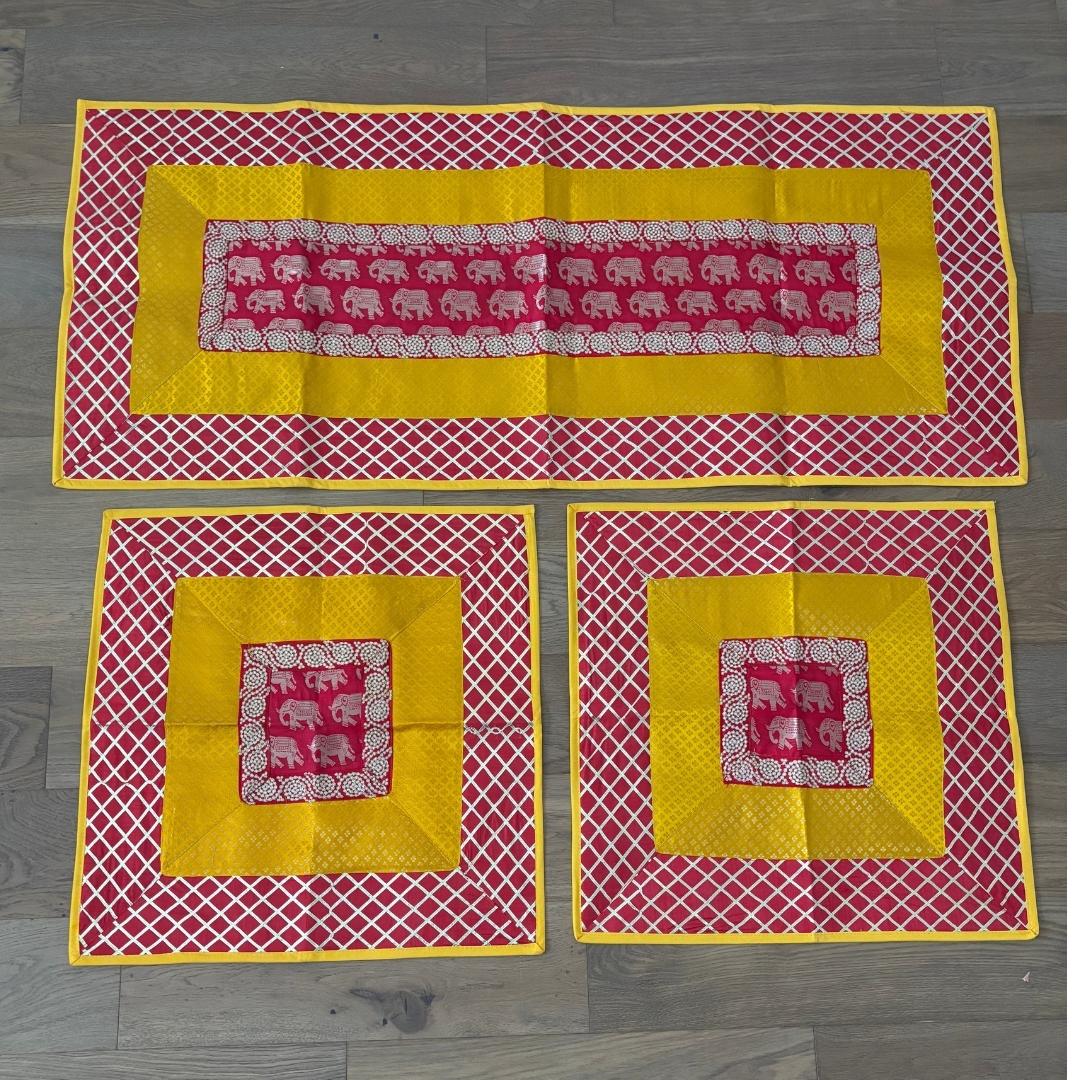 Handcrafted red-yellow elephant motif runner in silk brocade, large and small aasan mats layered for festive Ganesh setup.