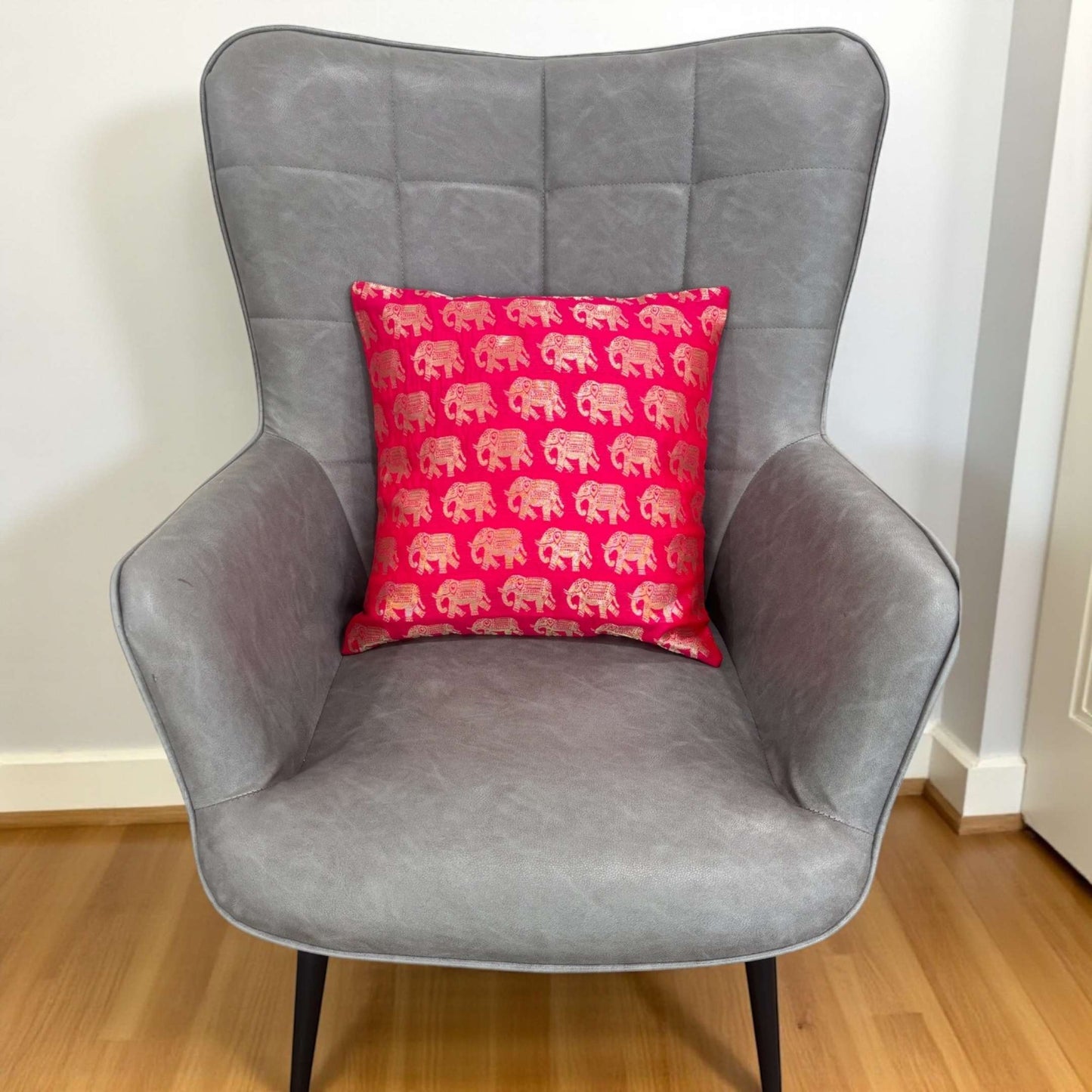 Gray armchair with a red pillow featuring pink elephants on a wooden floor.