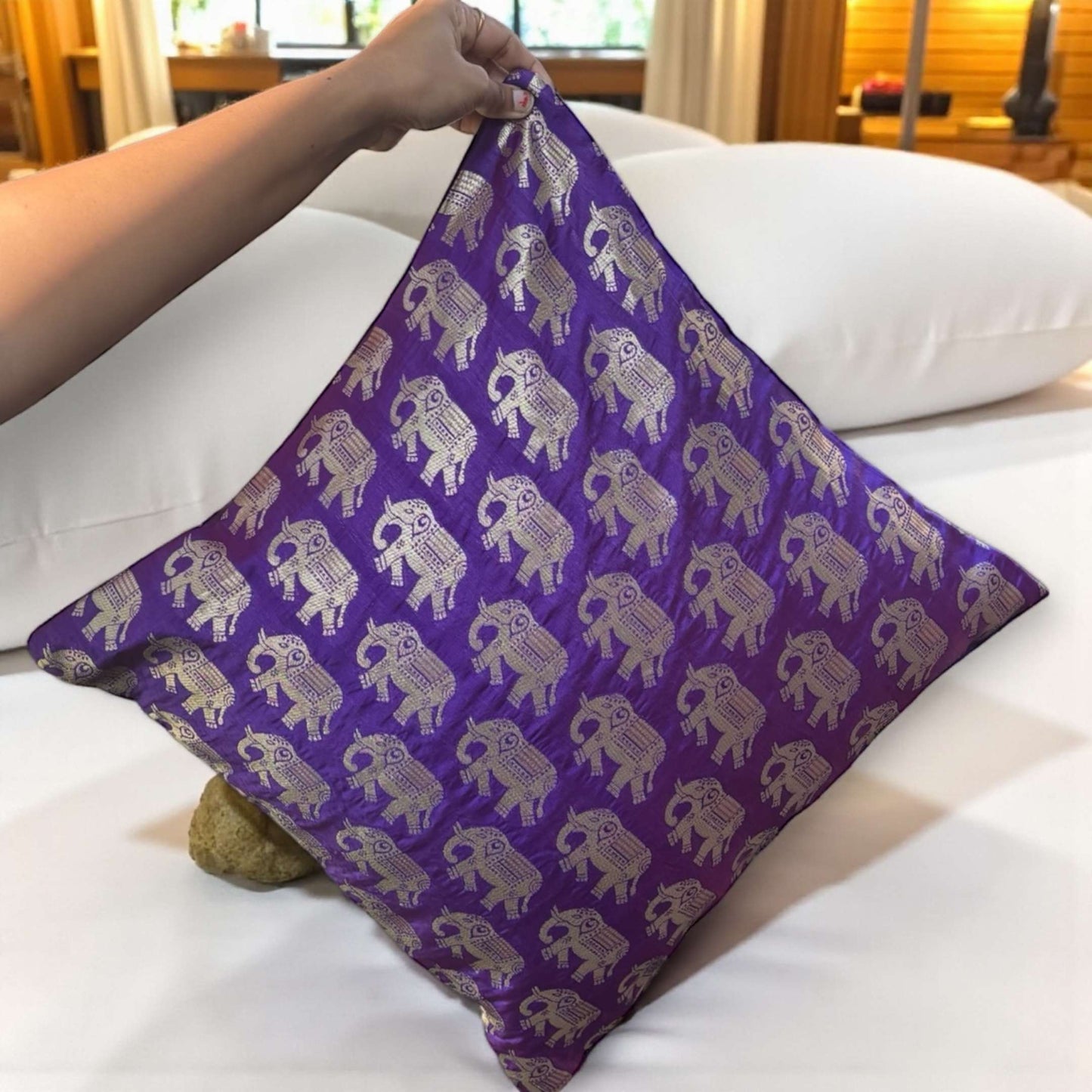 Purple pillow with elephant pattern held by a person on a white couch.