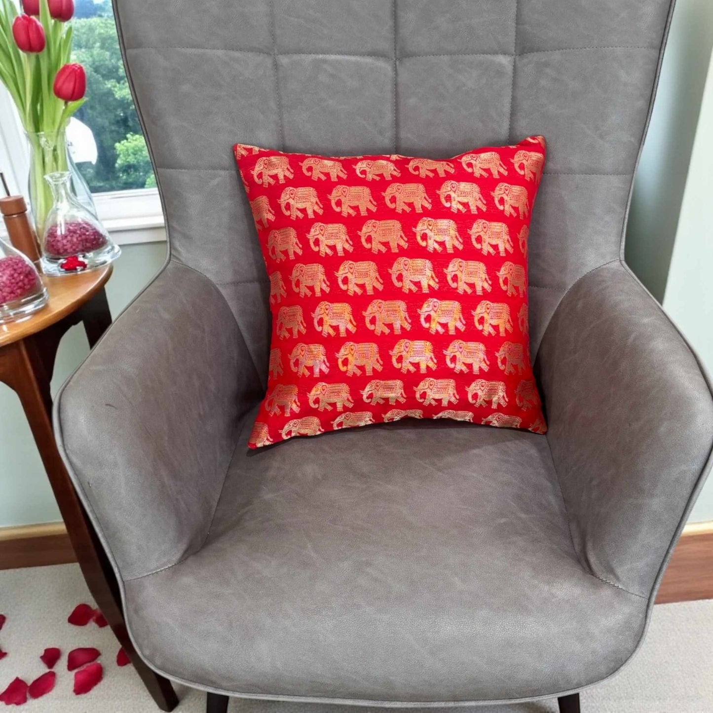 Red pillow with elephant pattern on a gray armchair in a room with a window and decor.