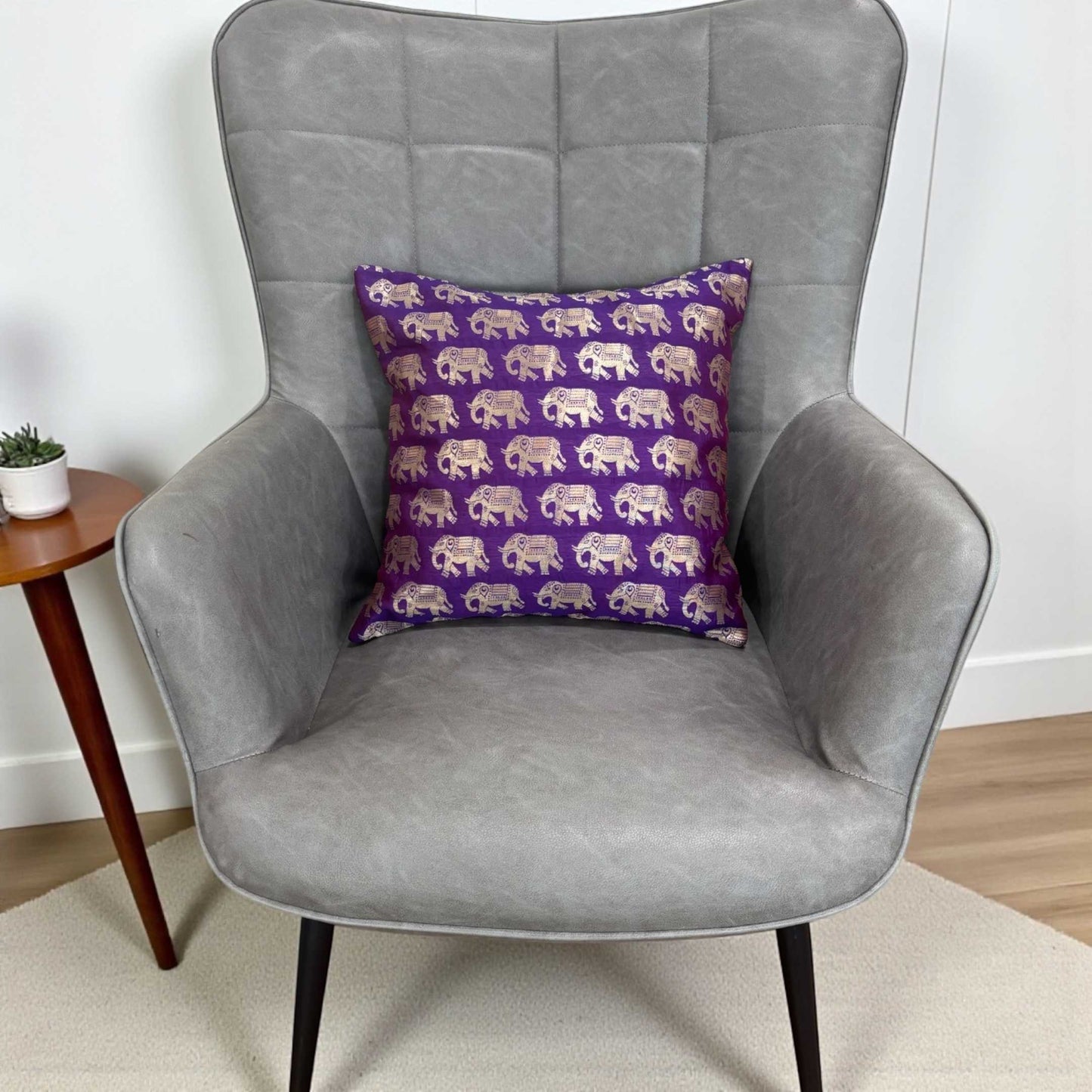 Gray armchair with a purple pillow featuring elephant patterns on a light wooden floor.