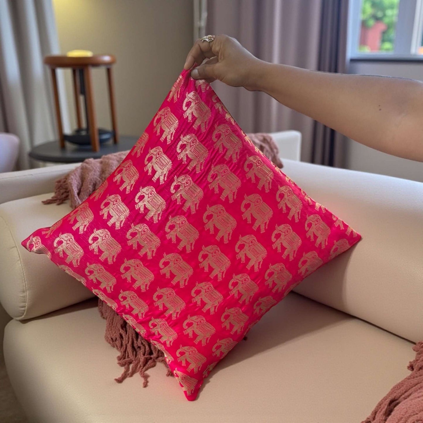 Person holding a pink pillow with elephant patterns on a beige sofa.