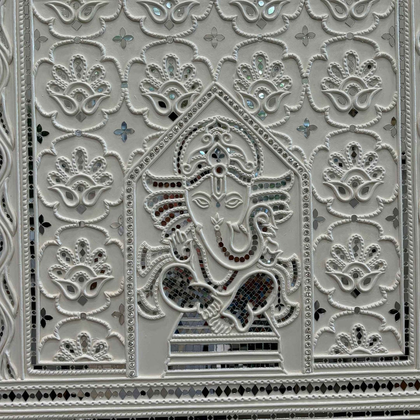 Decorative panel with intricate patterns and a central figure, likely a deity, on a white background.