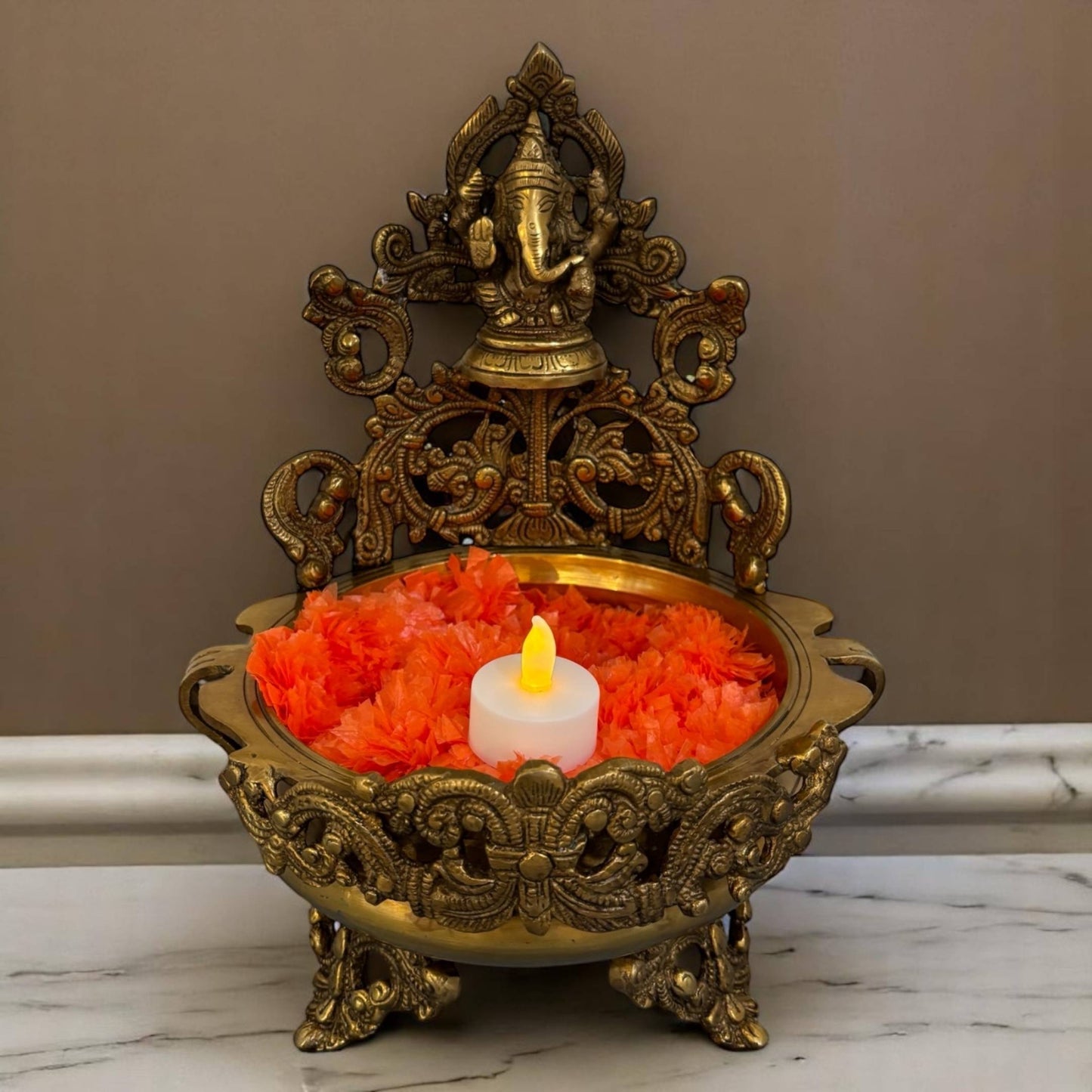 front view of the handcrafted brass Ganesha idol atop the Traditional Brass Ganesh Urli Bowl, showcasing intricate detailing suitable for diya stand urli and festive home decor