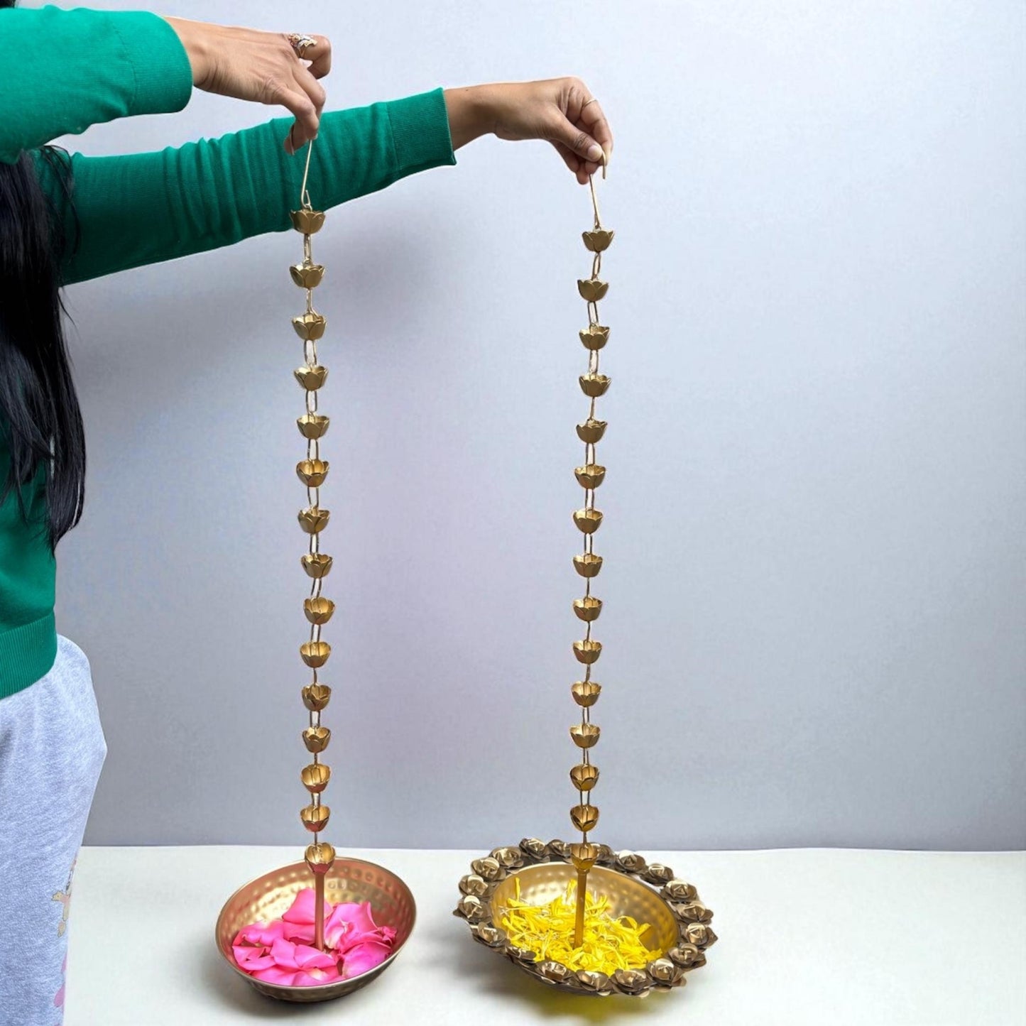 Urli Utsav Decor team holding two long, decorative hanging urlis with floral petals inside against a plain background