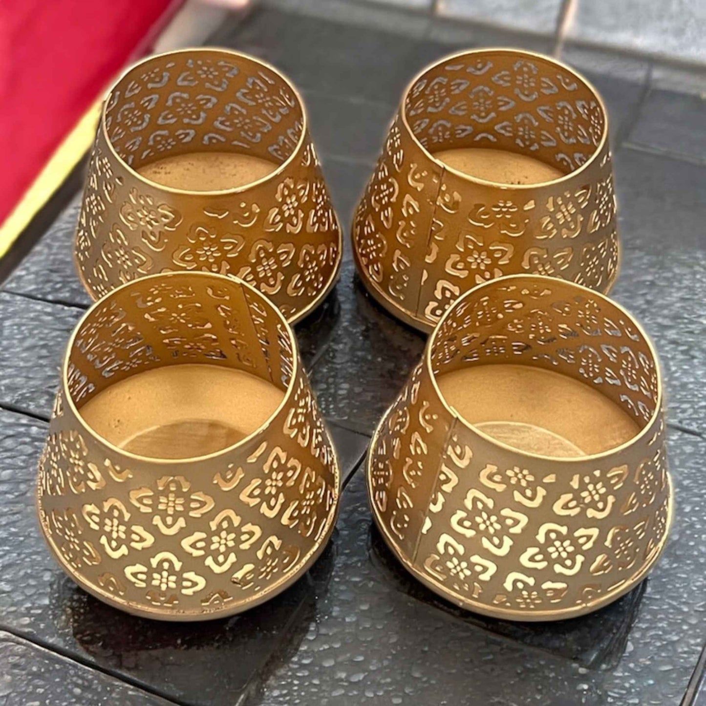 Four gold ornate t-lights on a dark surface
