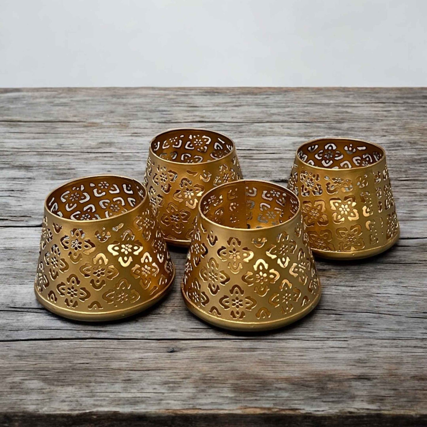 Four gold metal candle holders with intricate patterns on a wooden surface.