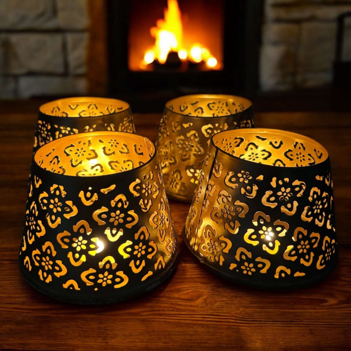 Decorative candle holders with floral patterns on a wooden surface in front of a fireplace.