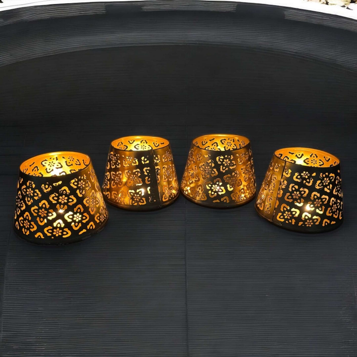 Four ornate metal candle holders on a black surface