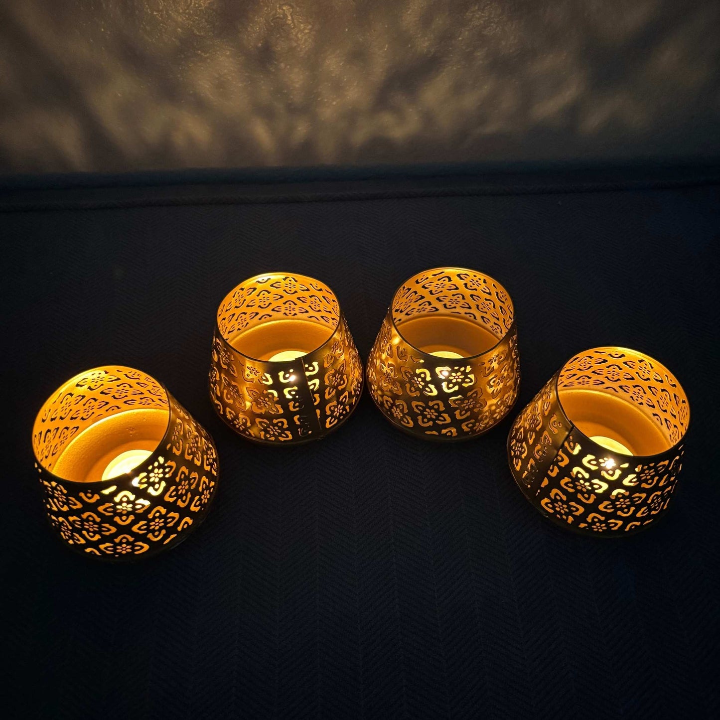 Four ornate gold candle holders with intricate designs on a dark background.