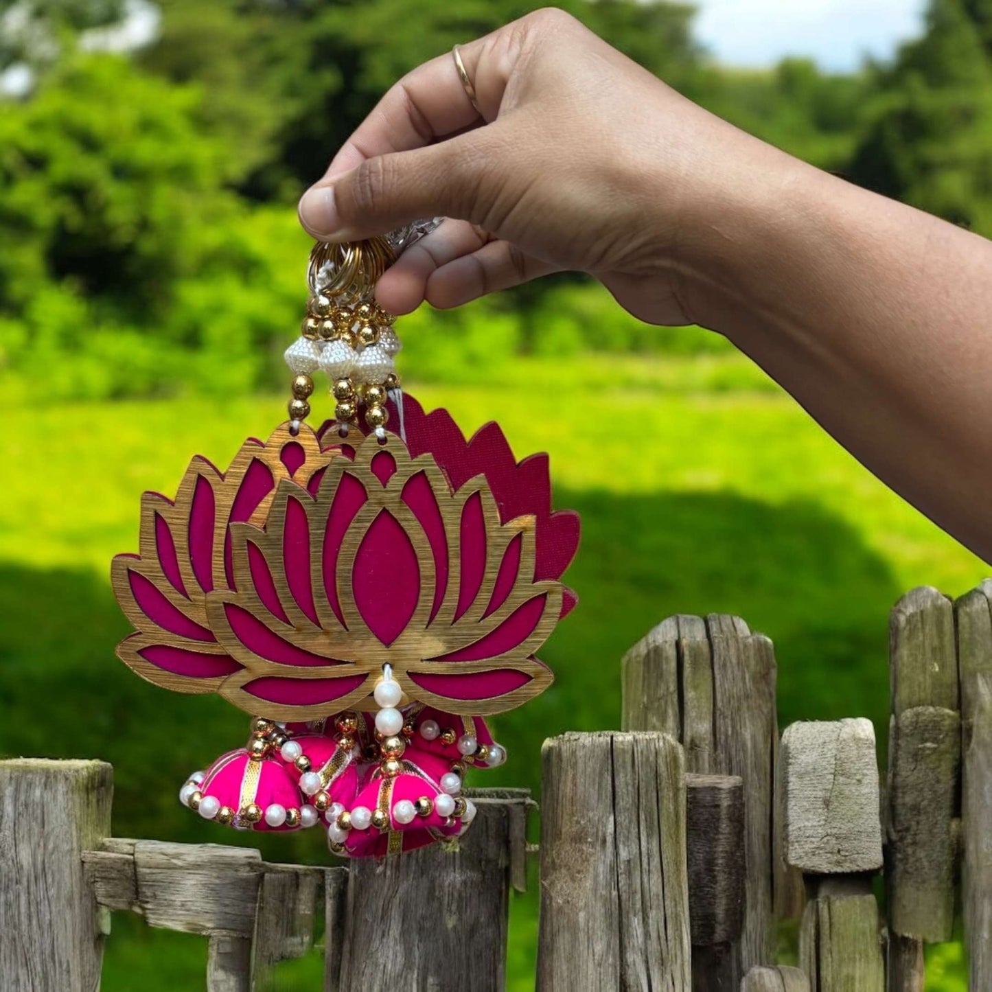 Hand holding a pink and gold decorative item resembling a lotus flower against a green outdoor background.