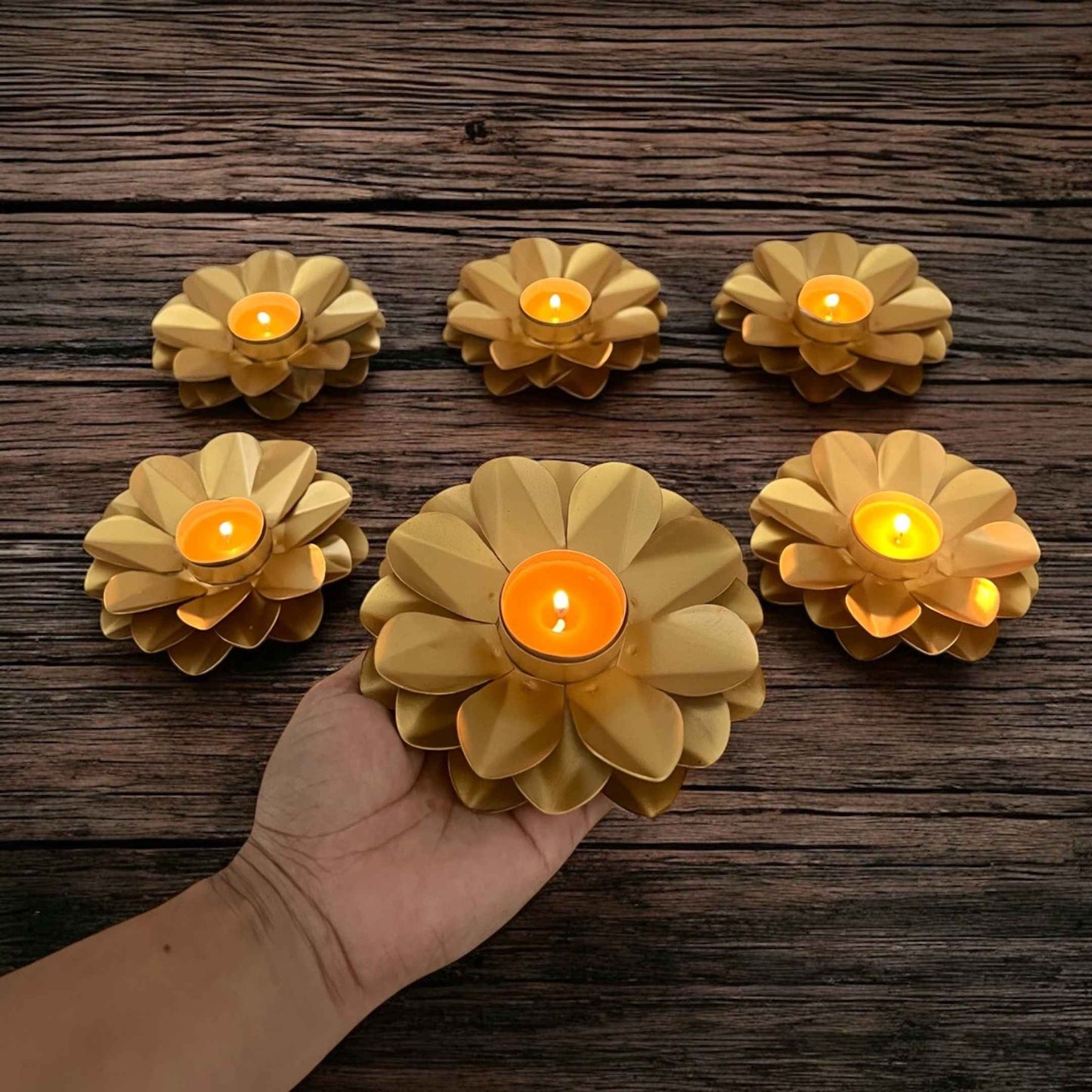 Set of six floral candle holders with lit candles on a wooden surface.