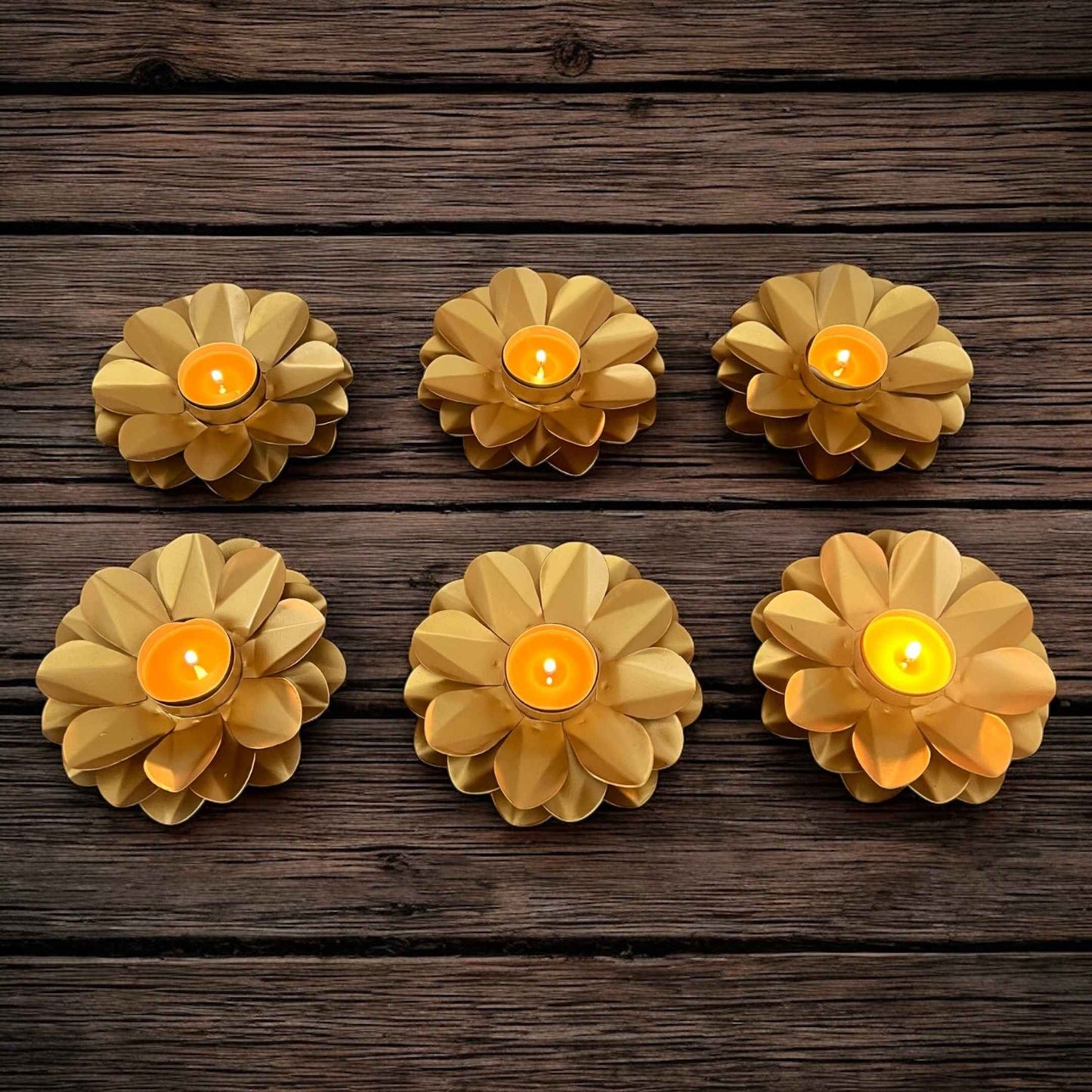 Six floral-shaped candles with lit candles on a wooden surface