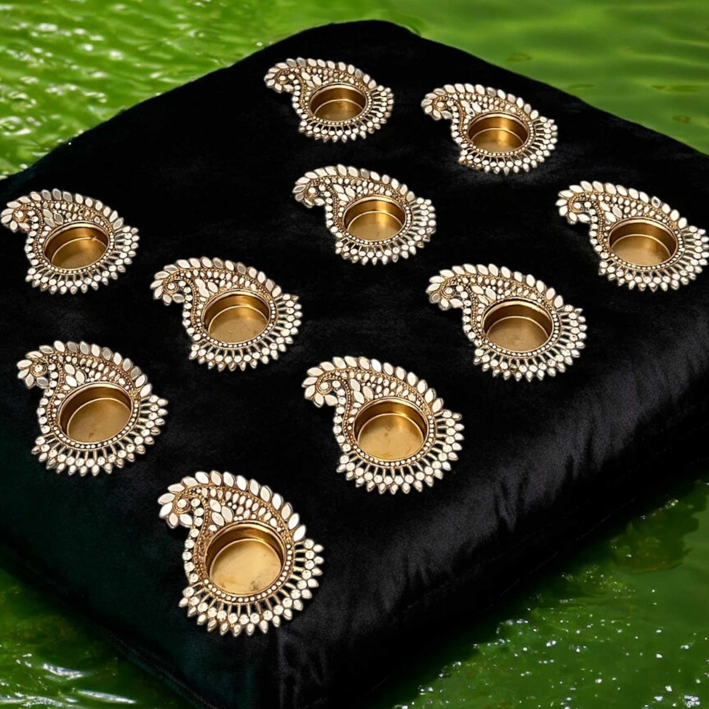 Mango paisley gold mirror Decorative gold candle holders on a black cushion with a green water background