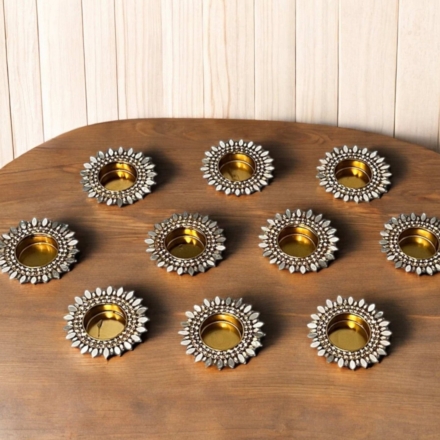 Sunflower shaped gold mirror decorative metal candle holders on a wooden board with a light wood panel background
