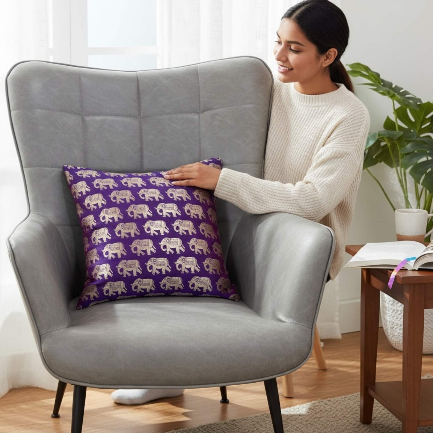 Woman holding a purple pillow with elephant pattern on a gray armchair in a bright room.