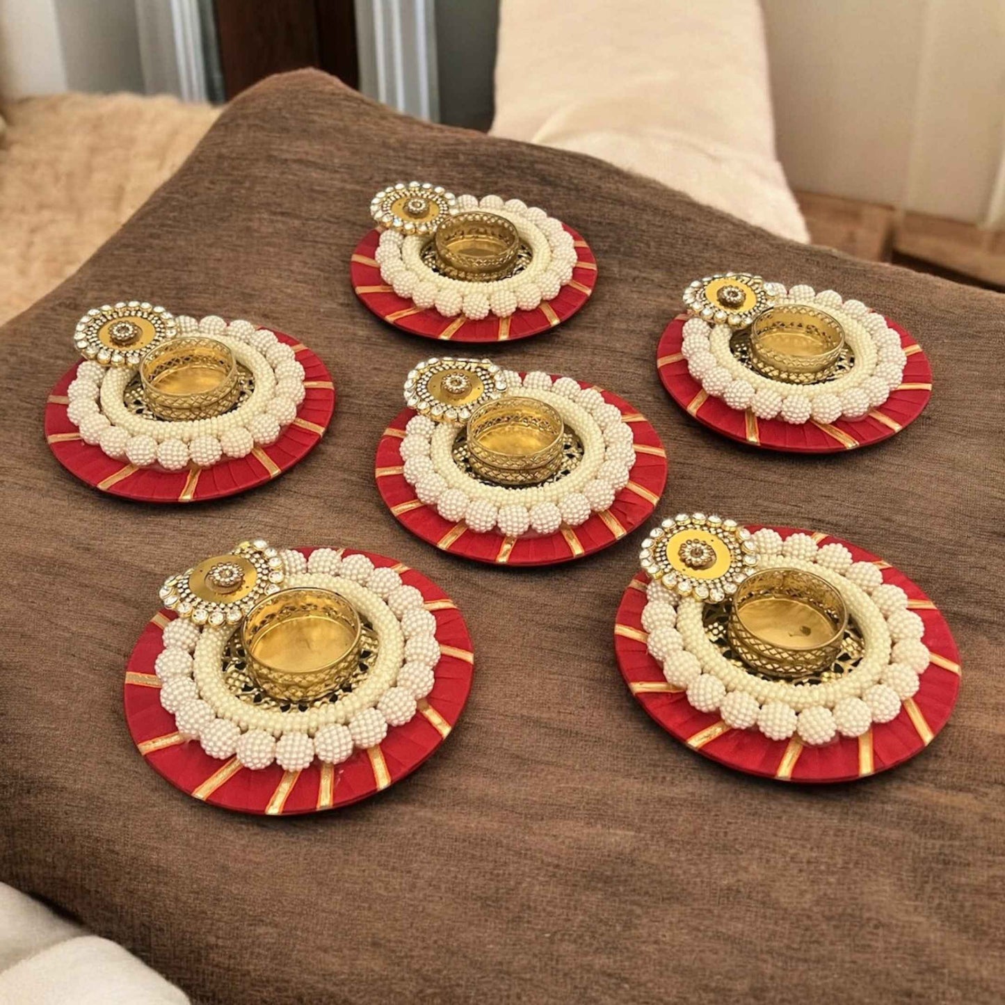 Decorative tea lights with gold and white center on red and gold circular bases on a brown surface.