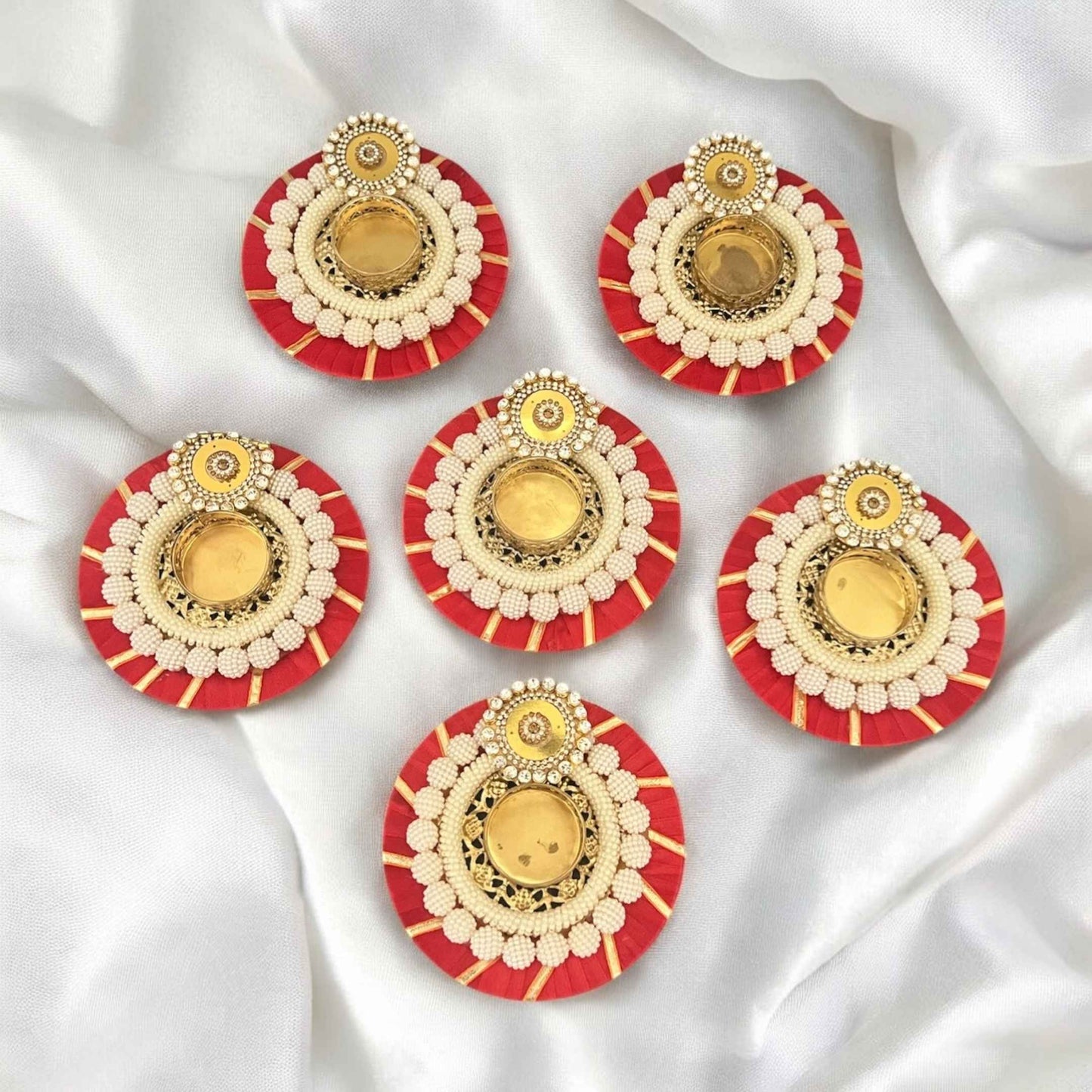 Set of six gold and red tea light holders on a white fabric background