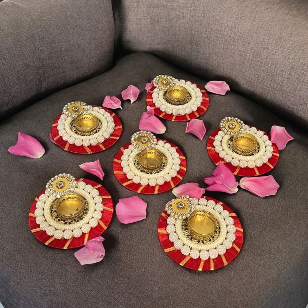 Decorative diyas with gold centers and red and white exteriors on a gray surface with pink petals.