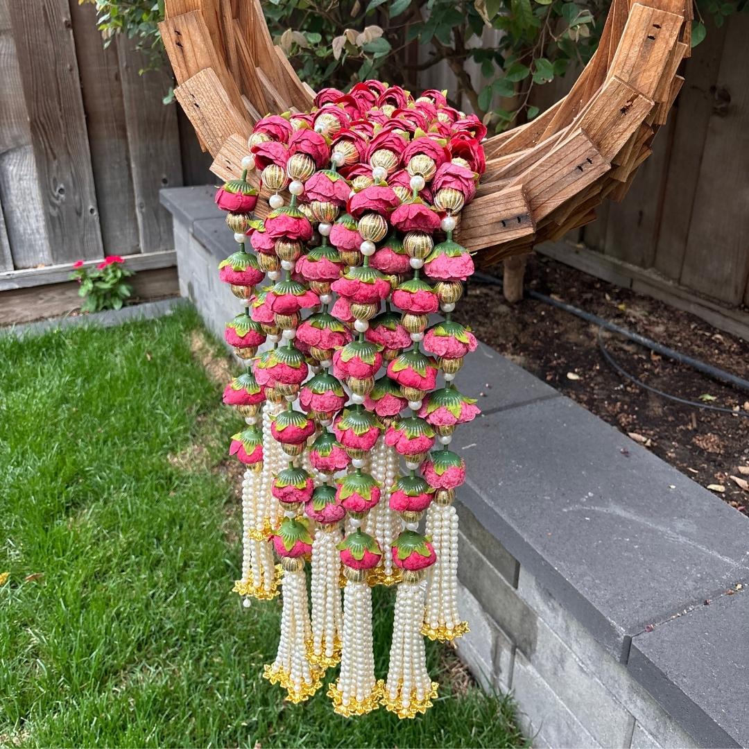 Decorative hanging garlands with red and gold flowers on a grassy area with a wooden structure in the background.