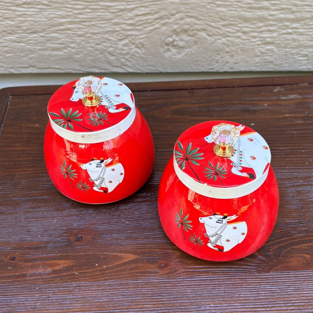 Two red metal jars with decorative lids on a wooden surface.