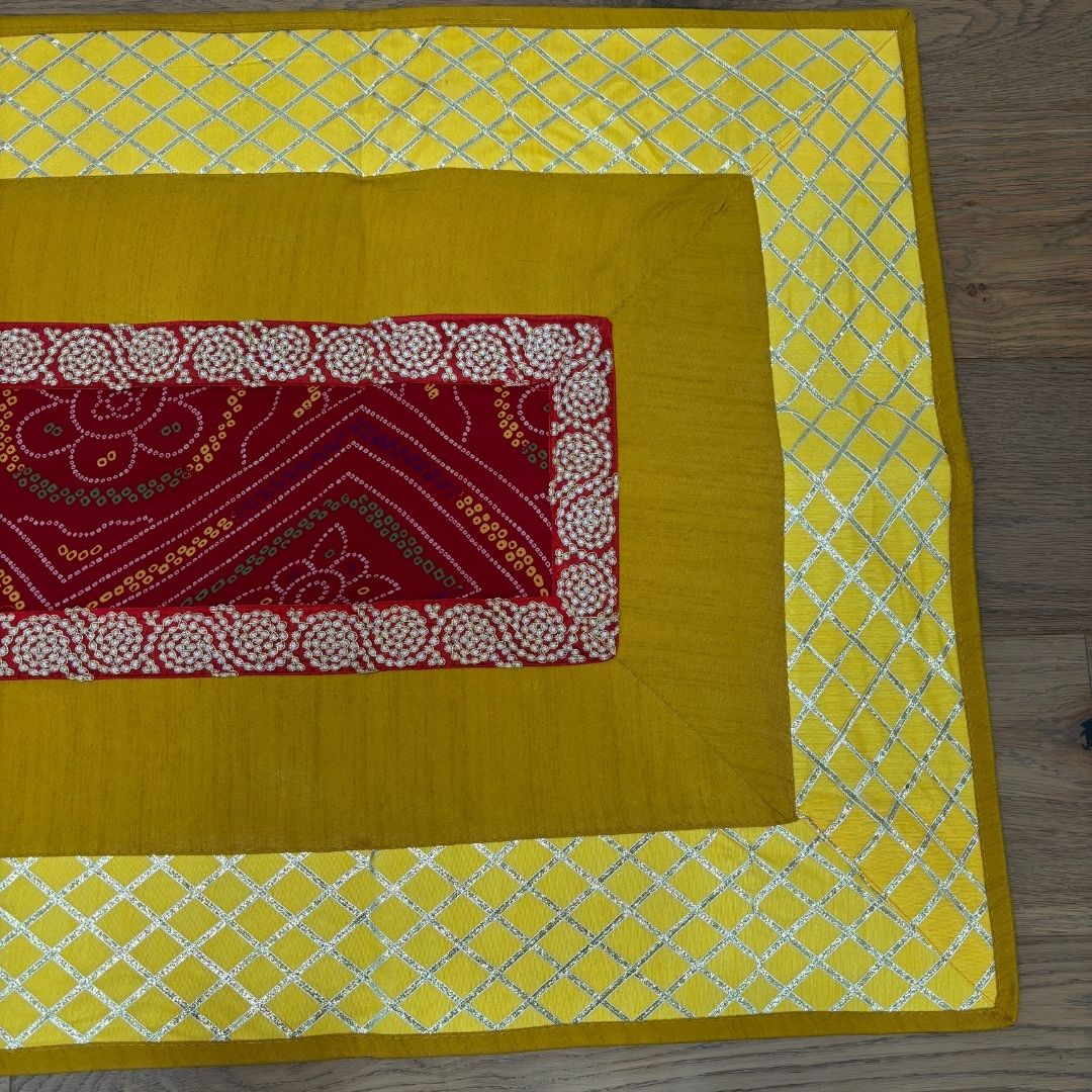 Yellow pooja aasan with red and white patterned square on a wooden surface
