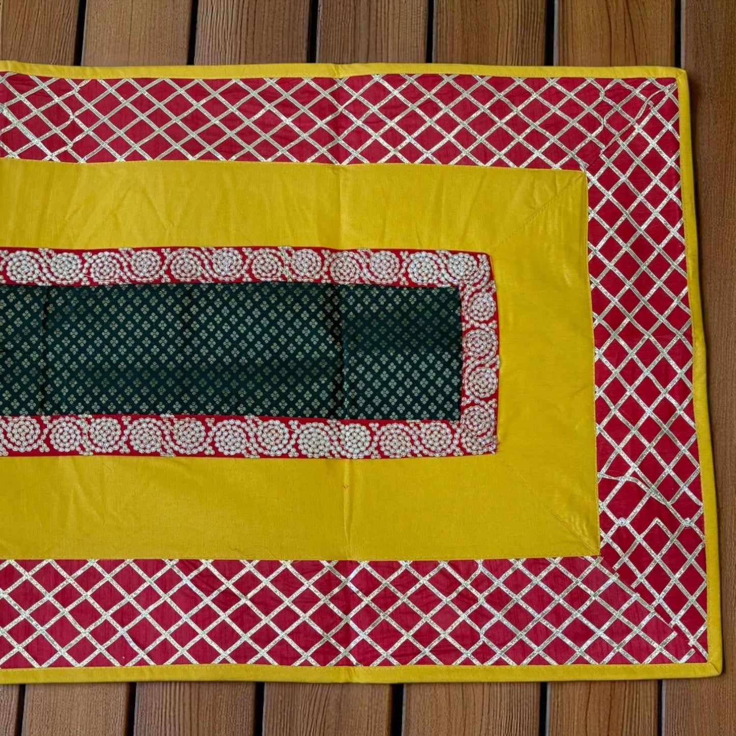 Close up of pooja aasan Fabric with red and yellow patterns on a wooden surface