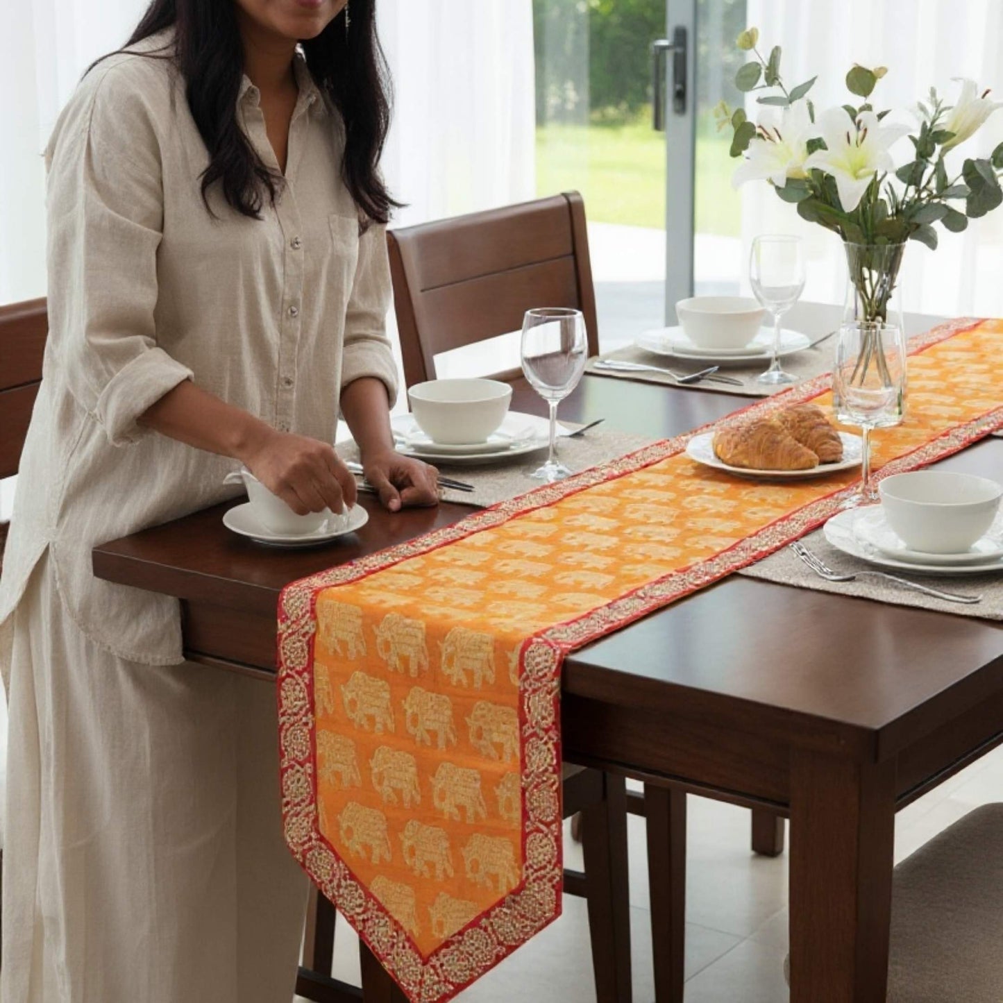 Woman setting a table with an orange table runner featuring elephant patterns.