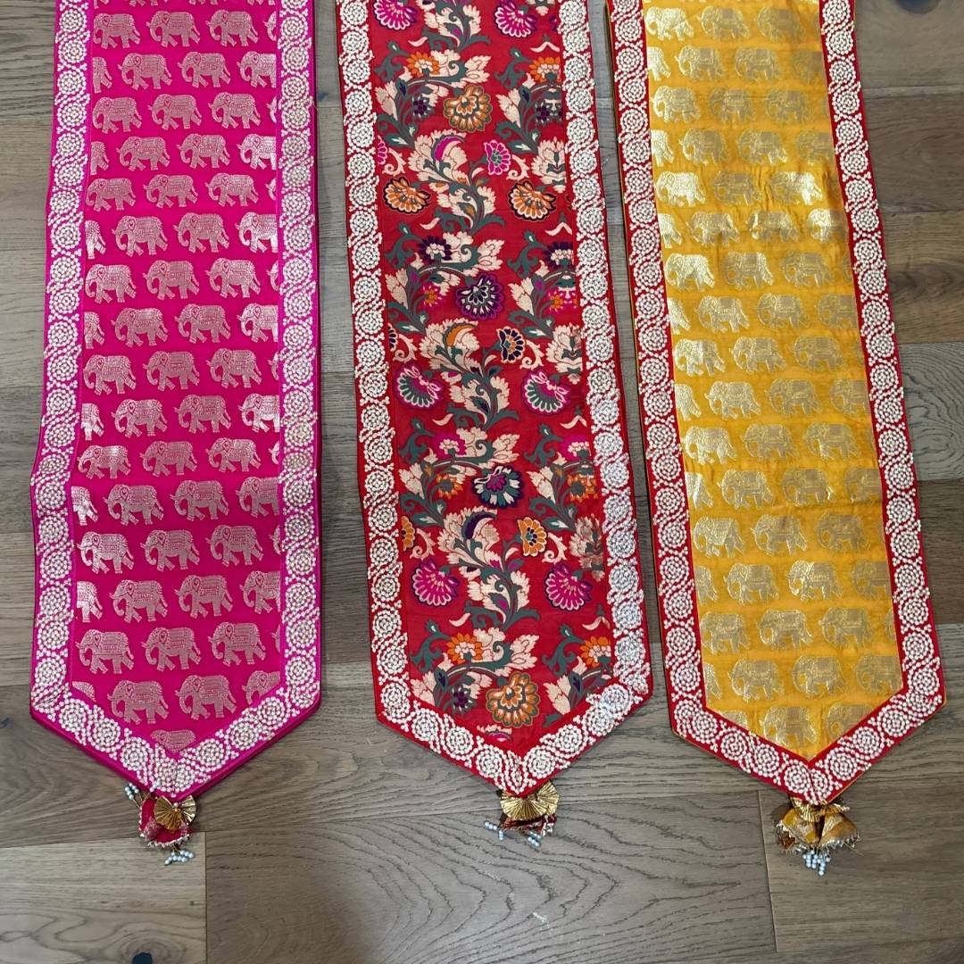 Three decorative table runners with elephant patterns on a wooden floor.