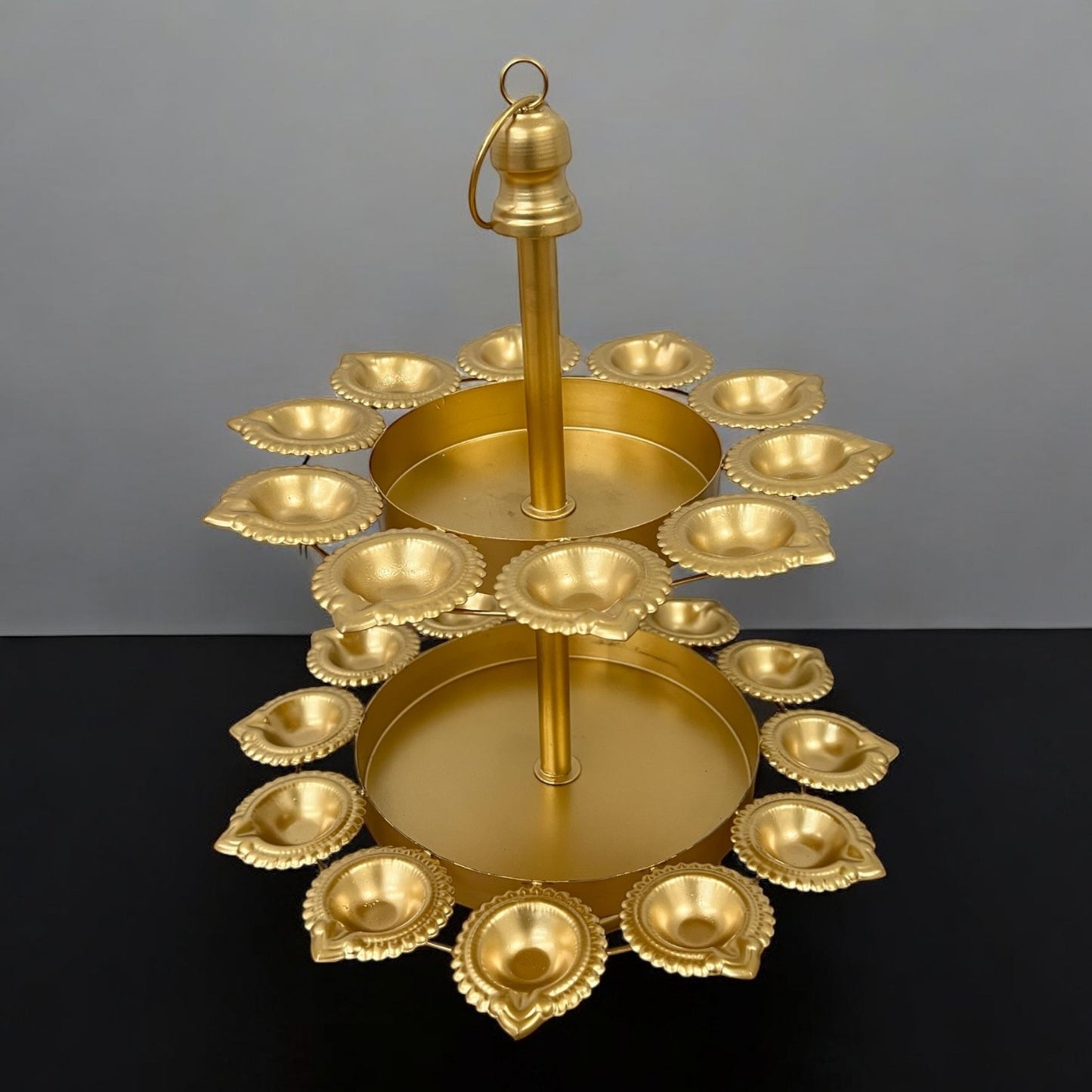 Urli Utsav Decor two‑layer gold finish diya urli displayed on dark stone surface, showing 18 unlit candle holders arranged in two concentric tiers with central hanging hook