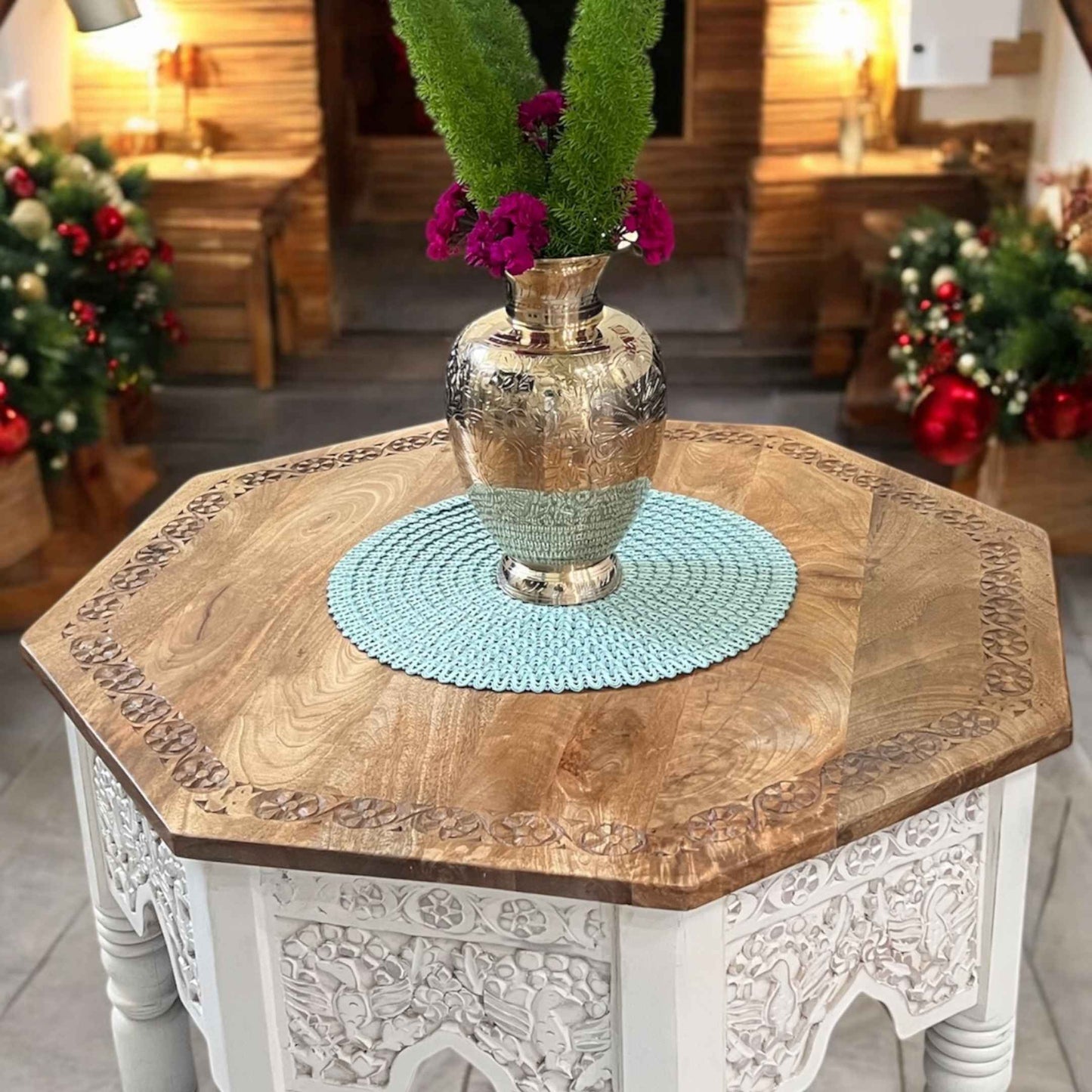 Handmade brass vase adorned with fresh flowers, placed on a wooden table in a cozy living room