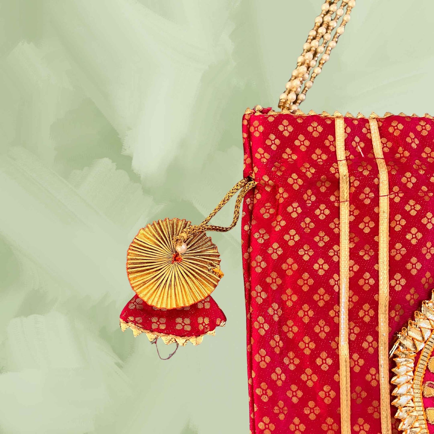 Red potli with gold patterns and a decorative gold item on a light green background